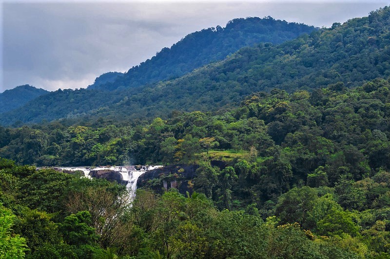 Photograph of the top of the Athirappilly waterfalls, surrounded by forested hilltops.