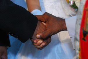 image of the close-up of a priest holding the hands of a newly married couple.