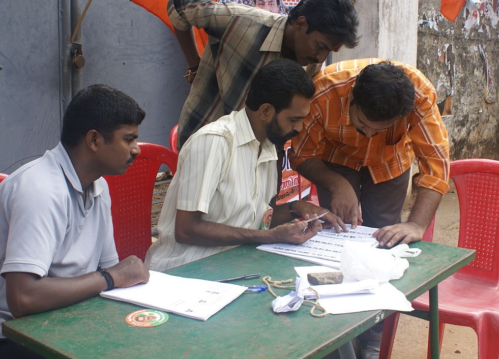 Four men look up a voter list at a table.